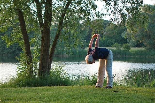 An elderly man stretches by a lake.